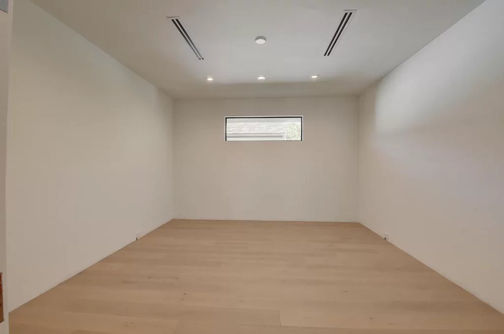 A minimalist empty room with wooden floors, white walls, and a narrow horizontal window.