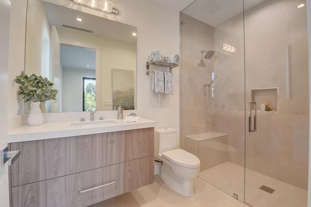 Modern bathroom with a glass shower, wooden vanity, and a view of outside foliage.