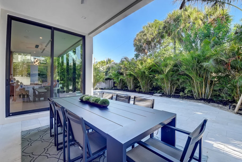 Outdoor patio dining area with a modern table and chairs set against a backdrop of lush greenery.