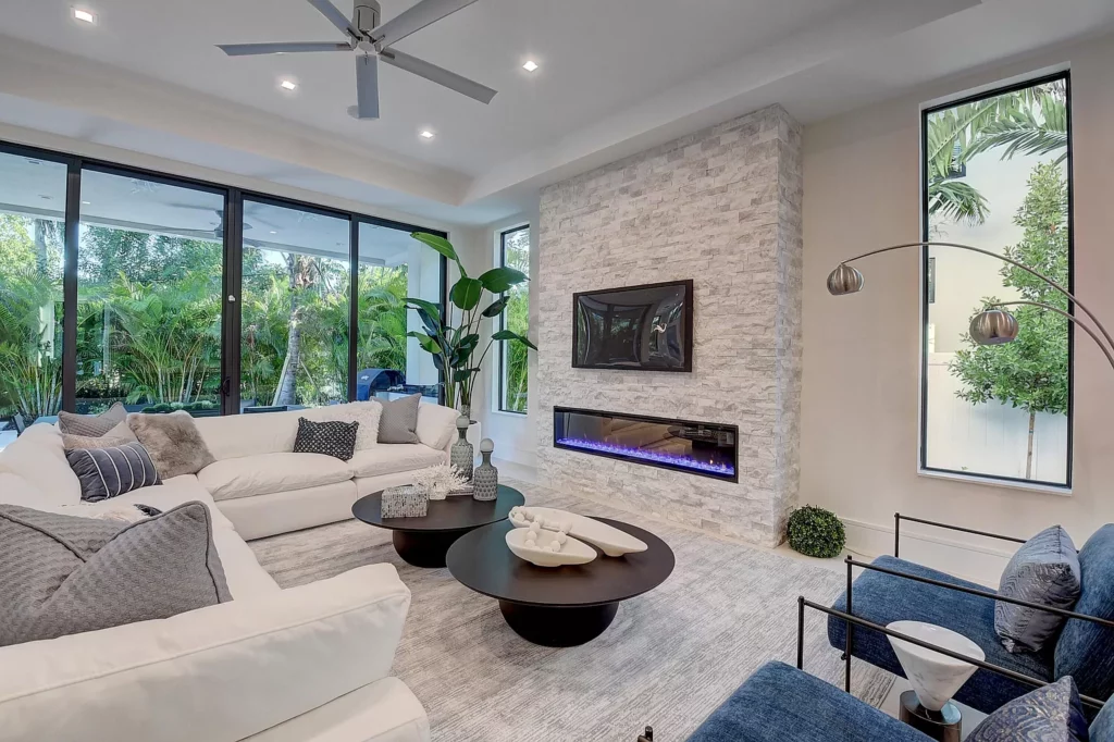 Modern living room interior with stone fireplace and large windows overlooking greenery.