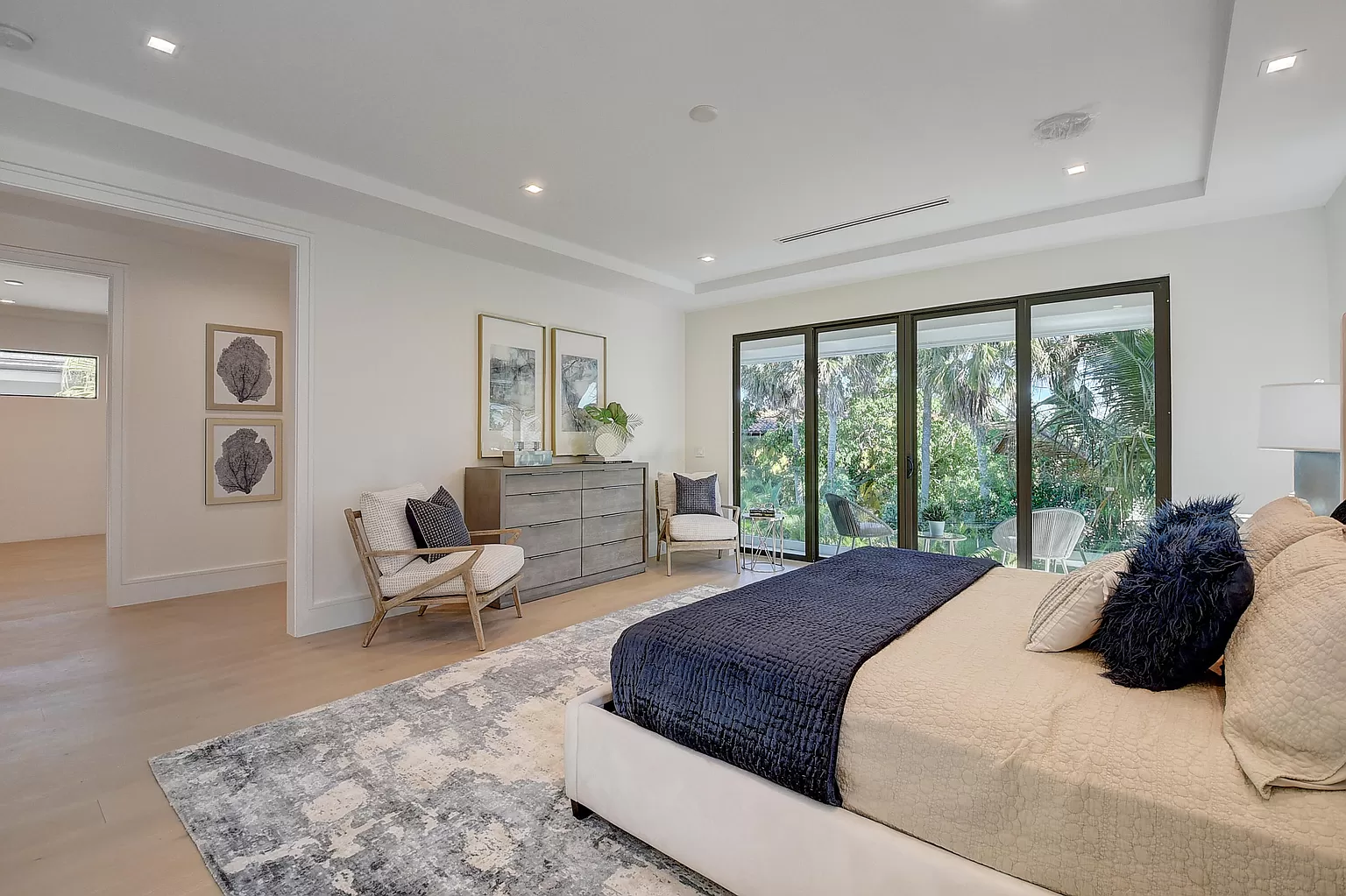 Modern bedroom with a king-sized bed, neutral color palette, and sliding glass doors leading to a lush outdoor view.