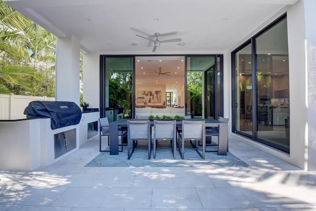 An outdoor dining area with a table set for six, adjacent to an open-concept interior living space.