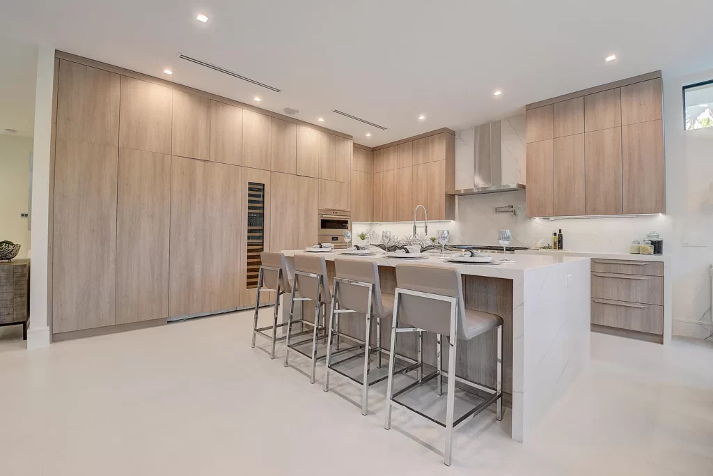 Modern kitchen with a minimalist design, featuring sleek wooden cabinetry, integrated appliances, and a central island with bar stools.