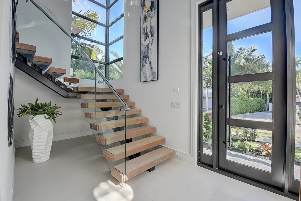 Modern staircase with wooden steps and glass railing in a bright, airy home entrance.