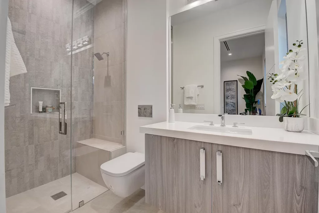 Modern bathroom interior featuring a glass-enclosed shower, wall-mounted toilet, and double sink vanity with large mirror.