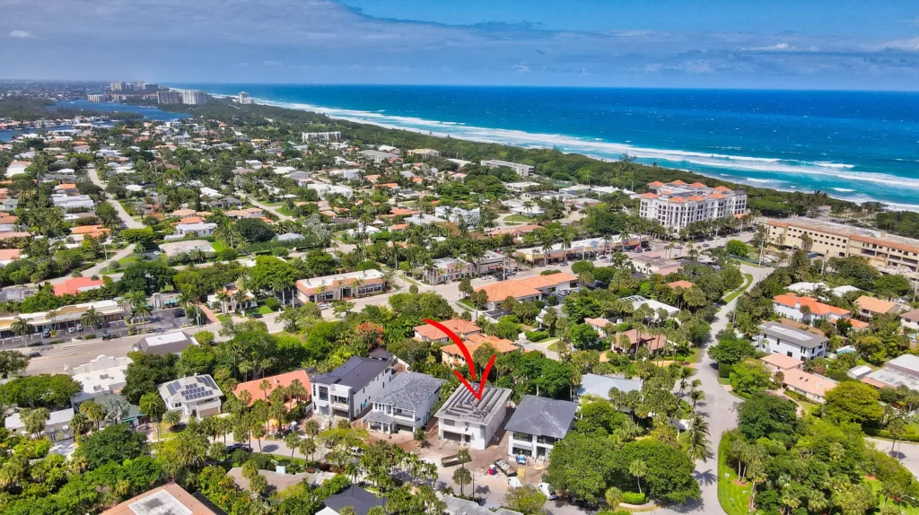 Aerial view of a coastal town with a red arrow pointing at a specific building near the beach.