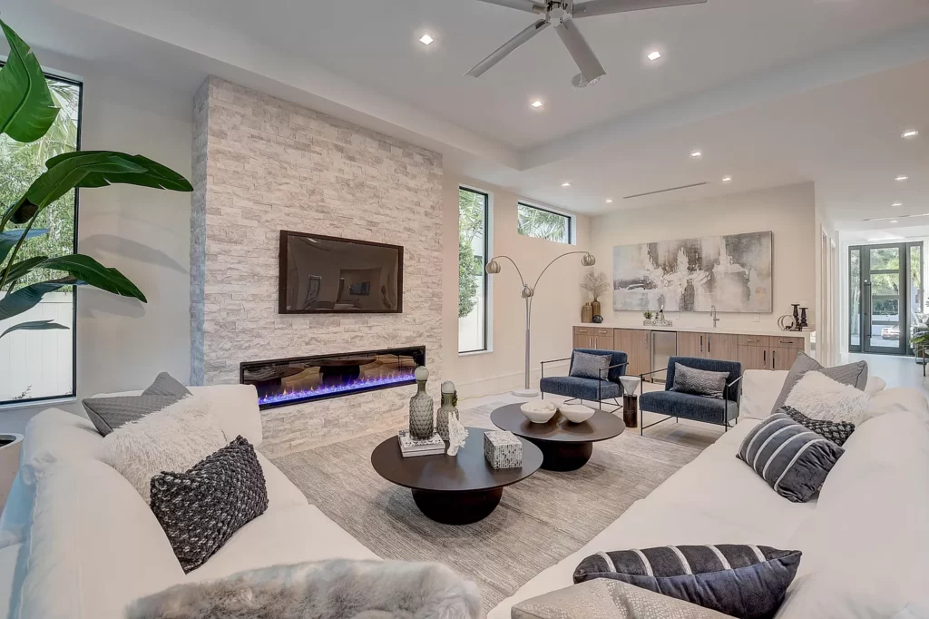 Modern living room with white sofas, stone fireplace, and a blue led light accent.